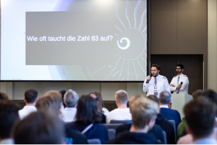 Vortrag in einem Seminarraum. Zwei Referenten der Firma AET in Piloten-Uniform halten vor einer Leinwand einen Vortrag.